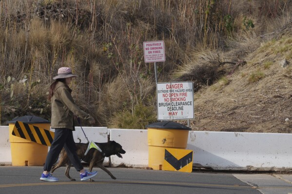 A Duarte resident walks her dog past a sign of an extreme fire hazard area Friday, Jan. 31, 2025, in Duarte, Calif. (AP Photo/Damian Dovarganes)